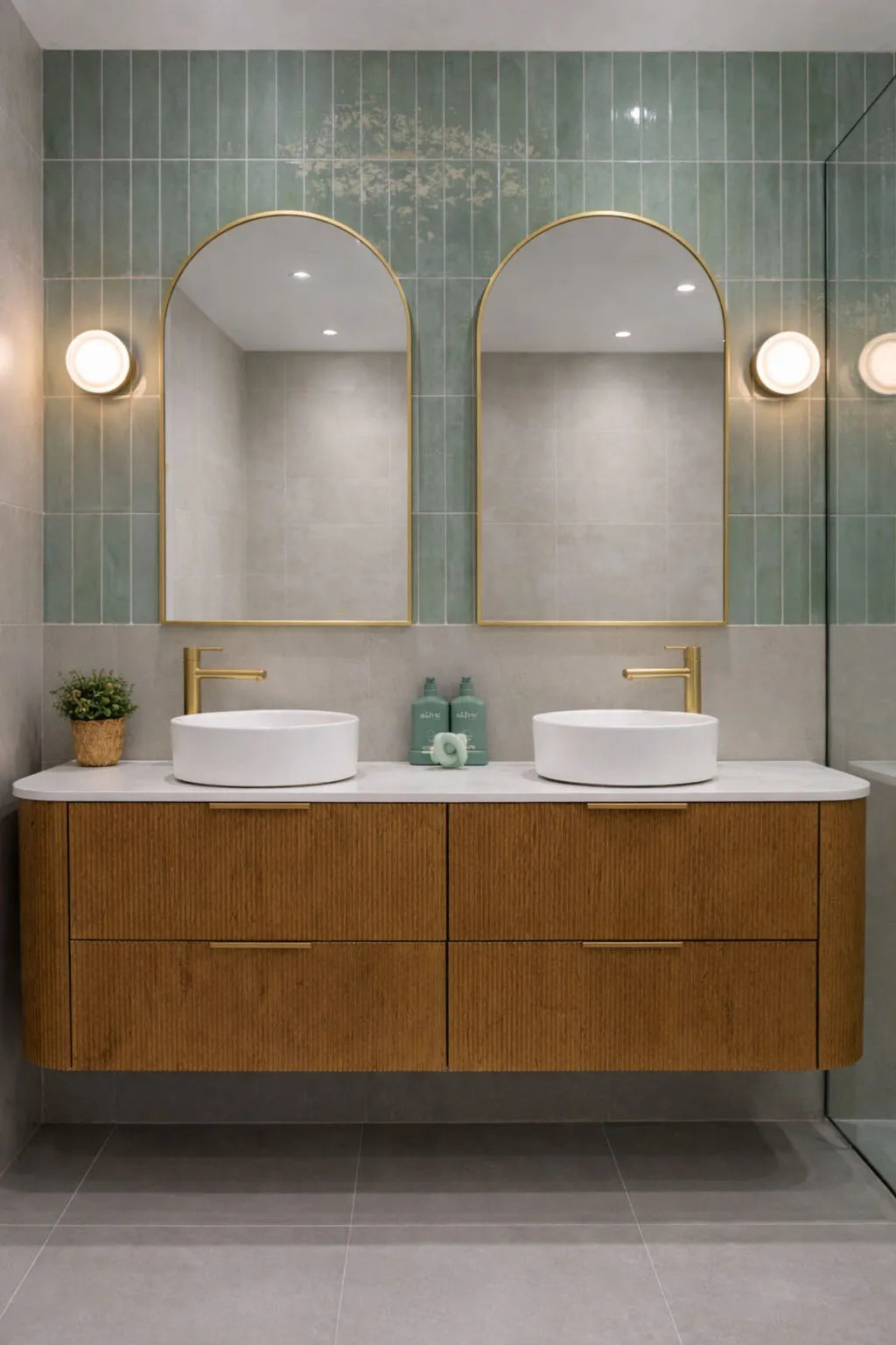 Bathroom vanity with wooden cabinets, white sinks, and gold fixtures against a green tiled wall.